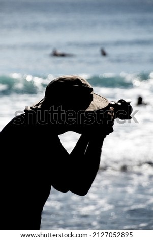 Photographer silhouette with sunshine on the hat brim in front of a beach with waves people swimming in Boca effect background