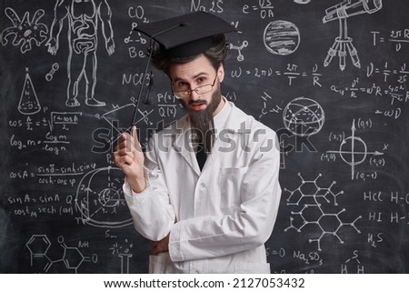 Science and education. A smart enthusiastic professor stands at the blackboard with scientific formulas and diagrams holding a pointer and looking pensively at the camera.  Royalty-Free Stock Photo #2127053432