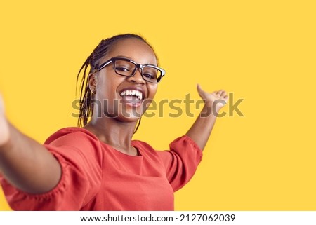 Happy cheerful confident black woman takes selfie, films tourist sightseeing view travel vlog or new home room tour, shares positive emotions, inviting welcoming gesture on empty blank mockup backdrop Royalty-Free Stock Photo #2127062039
