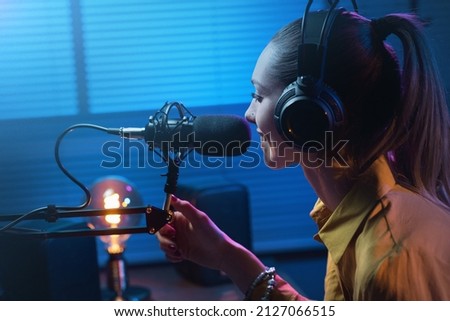 Young smiling woman wearing headphones and talking into a microphone at the radio studio, entertainment and communication concept