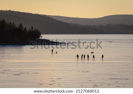 A Group of Silhouetted Young People Skate on the Frozen River at Sunset