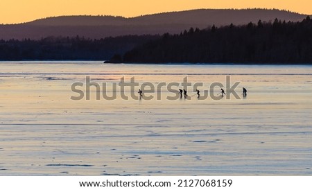 A Group of Teenage Boys in Hockey Gear Skate along the Frozen River at Sunset