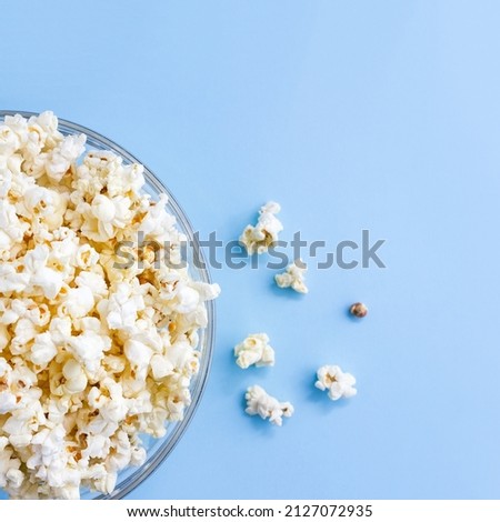 Popcorn in glass bowl on blue background. Top view, square banner. Selective focus, copy space