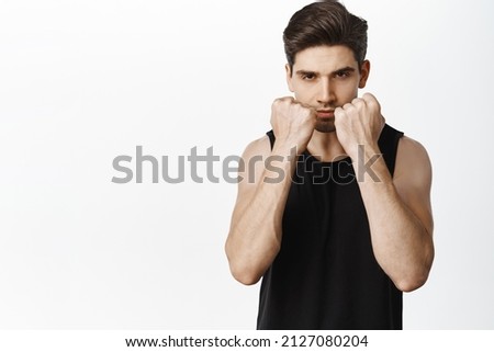 Portrait of sportsman fighter, standing in defensive boxing, wrestle pose, clench fists near head and looking determined, white background