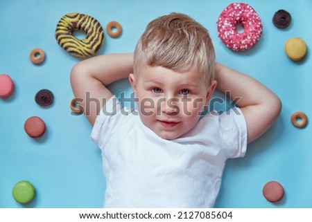 Cute smiling child on donuts and french macarons on blue background. National Donut Day concept. Happy childhood concept. Mock up white T-shirt.
