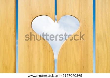 Hole in the fence in the form of a median. Concept and idea for a romantic picture. Wooden fence against a blue sky and a cloud. Photo for the design.