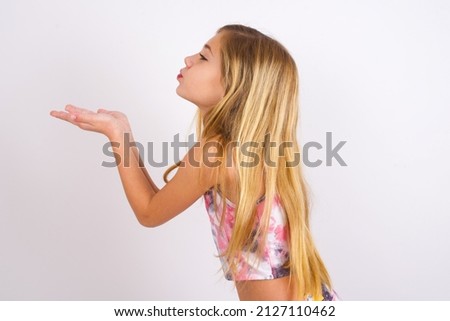 Profile side view view portrait of attractive little caucasian kid girl wearing sport clothing over white background sending air kiss