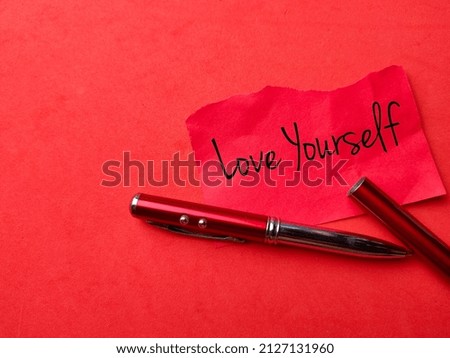 Top view pen and colored paper written with text Love yourself on a red background.