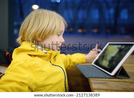Little boy is playing computer game or watching cartoon by tablet pc in a cafe.Parents are occuping the child to play while his food is cooking. Modern technology for education and entertainm