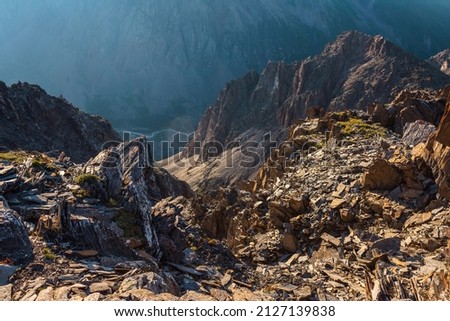 Awesome mountain view from cliff at very high altitude. Scenic landscape with beautiful sharp rocks near precipice and couloirs in sunlight. Beautiful mountain scenery on abyss edge with sharp stones. Royalty-Free Stock Photo #2127139838