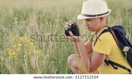 Happy boy, child dreams of becoming photographer. Child boy plays with camera, photographs flowers in summer park. Concept of childrens fantasy in nature. Child dreams of traveling, making discoveries