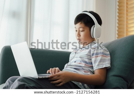 Asian little boy video call online via the internet tutor on a computer laptop with headphone. Homeschooling, Concept online learning at home 