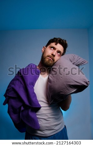 Miserable man with blanket and pillow after sleepless night, looking up and standing, copy space above  Royalty-Free Stock Photo #2127164303