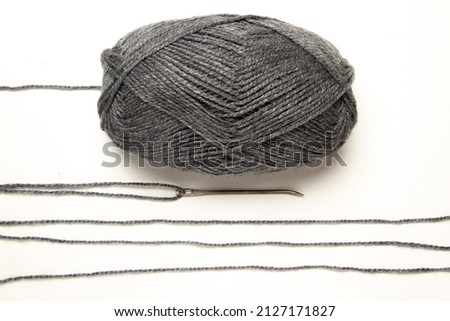 Gray wool ball with strips of wool on old needle on white table