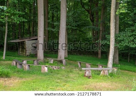 no people in this image of a woodland nature retreat with a circle of benches around a fire pit under tall woodland treees. Serene meditation setting. Royalty-Free Stock Photo #2127178871