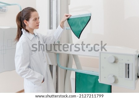 Hospital Radiology Room. Xray machine for fluorography. Doctor radiologist in gown adjusting the X-ray machine for radiography. Medical equipment. Scanning chest, heart or lungs in clinic office.