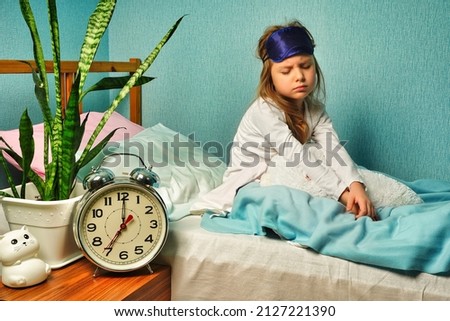 Dissatisfied upset child girl schoolgirl in white pajamas woke up early in the morning, does not want to get up Royalty-Free Stock Photo #2127221390
