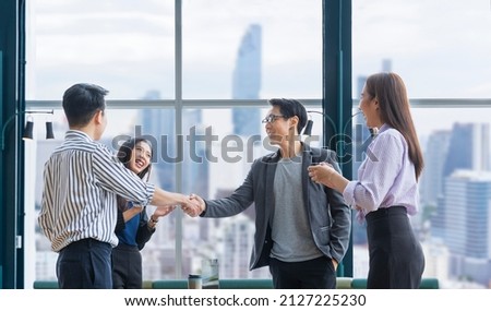 Asian business team leader congratulate his teammate employee for the outstanding achievement team performance by shaking hand in the modern office workplace with skyscraper view Royalty-Free Stock Photo #2127225230