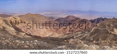 Multicolored desert landscape in Eilat mountains, Israel. Red and orange mountain ranges, chain of black volcanic mountains. Jordanian mountains at the background.                               Royalty-Free Stock Photo #2127237860