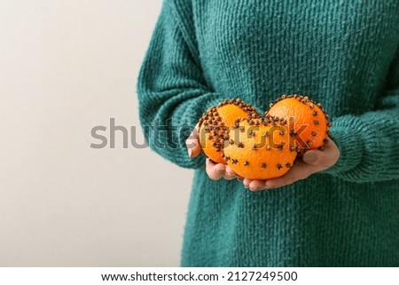 Woman holding handmade Christmas decoration made of tangerine with cloves on light background
