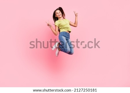 Photo of friendly lady jump show v-signs have fun wear green top jeans footwear isolated pink color background