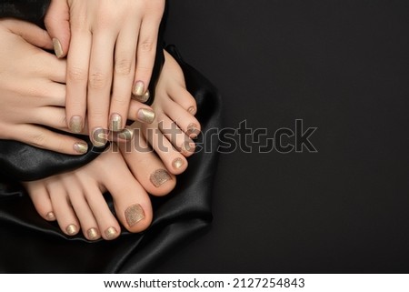 Female hands with golden nail design. Glitter gold nail polish pedicure. Female hands and feet with black fabric on black background. Copy space