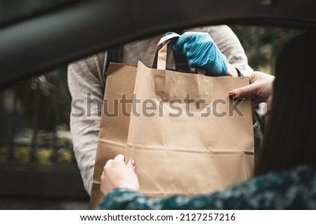Woman hand receiving shopping brow paper bag out of car open window driving thru pickup from seller with blue glove - view from the car inside - room for text or copyspace Royalty-Free Stock Photo #2127257216