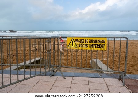 Weather alert - Storm warning: Yellow warning sign on a metal barrier prohibiting access to the beaches of the Atlantic coast with the message "Flood waves - Access prohibited" written in French