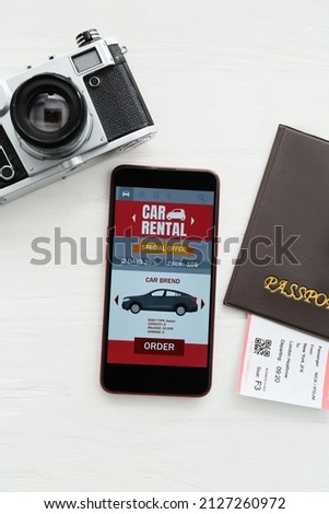 Mobile phone with open car rent app, passport and photo camera on white wooden background