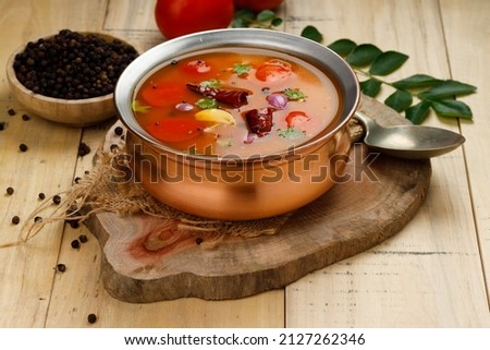 Rasam, south indians main item in meal, a veg soup which is very spicy-sweet-sour stock   which is traditionally arranged in a brass vessel with ingrediants beside it,wooden textured background.