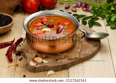 Rasam, south indians main item in meal, a veg soup which is very spicy-sweet-sour stock   which is traditionally arranged in a brass vessel with ingrediants beside it,wooden textured background.