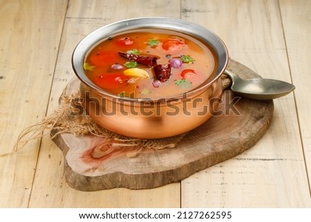 Rasam, south indians main item in meal, a veg soup which is very spicy-sweet-sour stock  which is traditionally arranged in a brass vessel with spoon beside it, wooden texture background