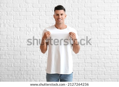 Handsome young man in stylish t-shirt on white brick background