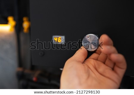 Male hand adjusting temperature on water gas heater of black colour. Close-up.