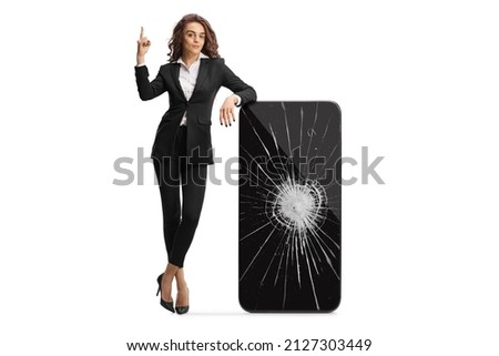 Businesswoman pointing up and leaning on a smartphone with a broken screen isolated on white background