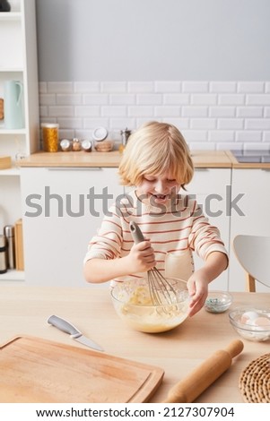 Vertical portrait of cute little boy baking sweets in cozy kitchen lit by sunlight