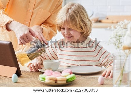 Portrait of cute smiling boy enjoying breakfast in kitchen and watching cartoons via laptop