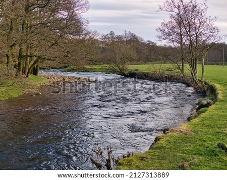A meander in the River Dunsop near Dunsop Bridge in Lancashire, UK. On the left rock debris on the slip-off slope is visible while on the right, lateral erosion has formed a small river cliff. Royalty-Free Stock Photo #2127313889