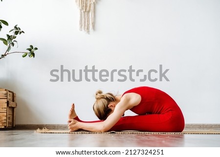 Lady in a red tracksuit performs yoga exercises.girl lies in a deep crease.Paschimottanasana.Tilt to the legs sitting. Complete relaxation,Yoga for mind and body.High quality photo Royalty-Free Stock Photo #2127324251