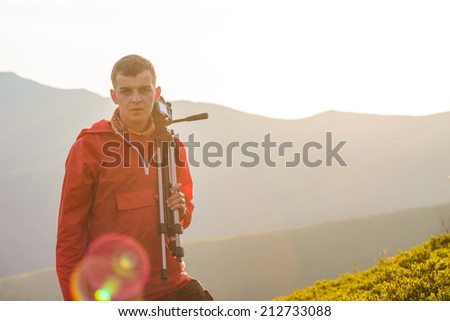 photographer holding a tripod and camera while looking out on mountain 