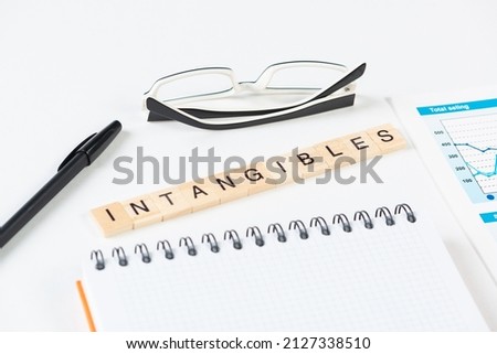 Intangibles concept with letters on wooden cubes. Still life of office workplace with supplies. Flat lay white surface with glasses, pen and notepad. Intellectual capital and property. Royalty-Free Stock Photo #2127338510