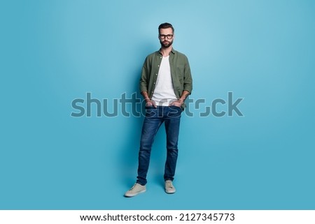 Photo of handsome smart focused cool guy posing wear green shirt jeans sneakers isolated blue color background