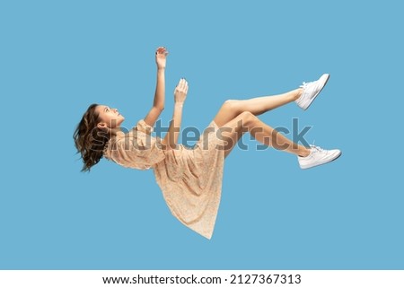 Floating in air. Relaxed girl in yellow dress levitating, looking up while flying mid-air, having comfortable peaceful dream. full length studio shot isolated on blue background, indoor Royalty-Free Stock Photo #2127367313