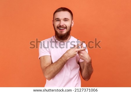 Hashtag gesture. Portrait of bearded man crossing fingers, showing hash symbol, tagging famous internet message, viral blog, wearing pink T-shirt. Indoor studio shot isolated on orange background.