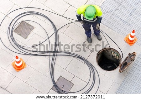electrician worker install optical fiber cable for internet and telephone underground lines  in city street Royalty-Free Stock Photo #2127372011