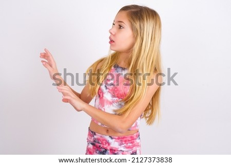 Displeased little caucasian kid girl wearing sport clothing over white background keeps hands towards empty space and asks not come closer sees something unpleasant