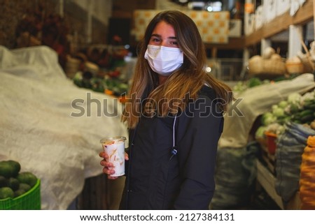 Portrait of a caucasian woman holding a fruit salad and standing in the middle of a fruit market. Horizontal. With copy space. Looking at the camera.