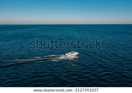 A view from a height of a white speedboat sailing in the birch sea. The motor boat leaves a mark on the water. The concept of water travel and recreation. Royalty-Free Stock Photo #2127391037