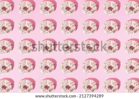 Arranged small ring donuts with white glaze and colorful crumbs on a pink pastel background. Pattern. Flat lay.