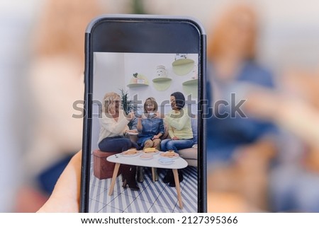 Female hands taking photo on smartphone of three women eat cakes together. Family having meal together